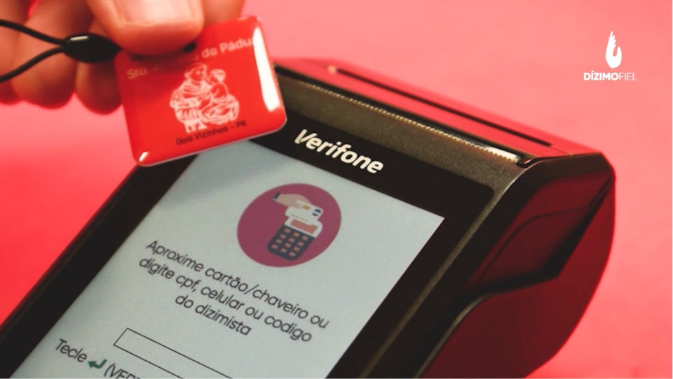 Pessoa aproximando um chaveiro na maquininha do dízimo